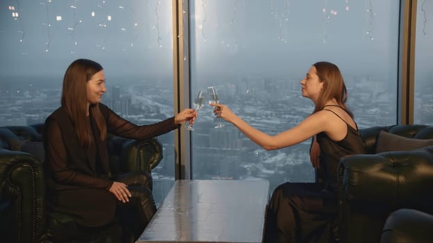 Attractive women clink glasses and drink champagne in restaurant. Media. Beautiful young women relax in champagne restaurant. Friends meet and celebrate with champagne in restaurant.