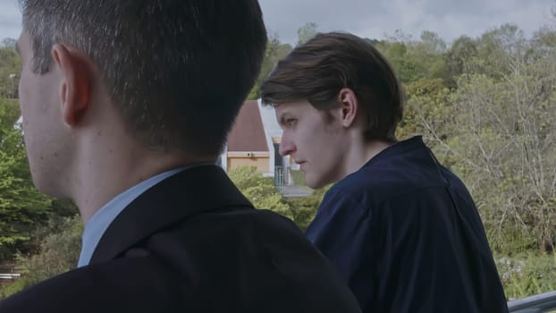 Two young men standing on balcony and communicating. Stock clip. Business partners discussion and green spring vegetating on the background