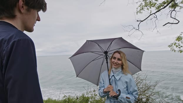 Young couple sharing a day at the beach during cold spring weather. Stock clip. Man and woman with umbrella meeting at the sea shore