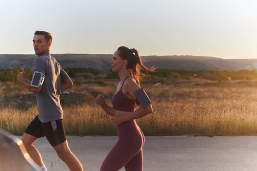 A handsome young couple running together during the early morning hours, with the mesmerizing sunrise casting a warm glow, symbolizing their shared love and vitality.