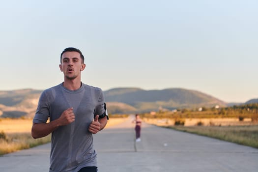 A handsome young couple running together during the early morning hours, with the mesmerizing sunrise casting a warm glow, symbolizing their shared love and vitality.