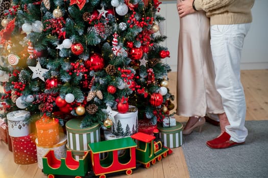 Romantic couple standing near Christmas tree at home and hugging.