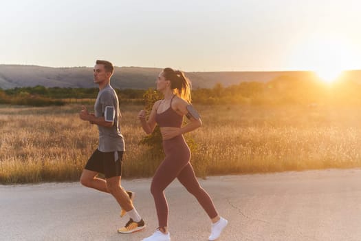 A handsome young couple running together during the early morning hours, with the mesmerizing sunrise casting a warm glow, symbolizing their shared love and vitality.