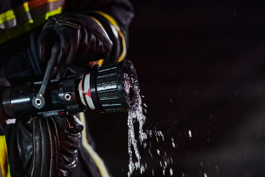 Firefighter using a water hose to eliminate a fire hazard. Team of firemen in the dangerous rescue mission