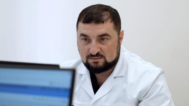 Middle aged doctor with in clinic. Clip. Bearded man in white coat looking at computer monitor