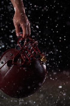 Close up of American Football Athlete Warrior Standing on a Field focus on his Helmet and Ready to Play. Player Preparing to Run, Attack and Score Touchdown. Rainy Night with Dramatic lens flare.