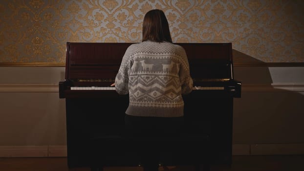 Young woman sits down to play piano. Media. Rear view of woman sitting down to play piano. Woman plays old piano.