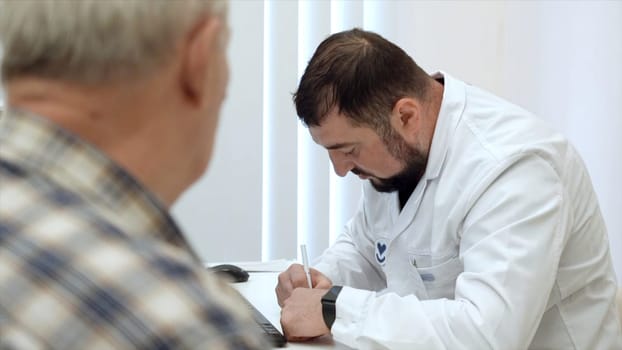 Senior male patient talking with man doctor in the office. Clip. Writing prescription to senior patient