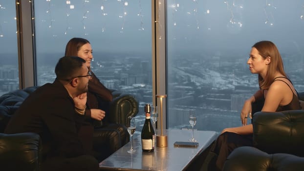 Group of friends are talking in restaurant. Media. Friends are chatting in company in restaurant. Three friends chat in restaurant on background of dark winter city.