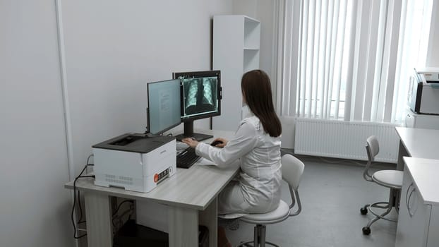 Female doctor looks at X-ray on computer. Clip. Doctor in bathrobe looks at tests and X-rays in computer room. Modern electronic technologies in medical clinics.
