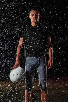 American Football Field: Lonely Athlete Warrior Standing on a Field Holds his Helmet and Ready to Play. Player Preparing to Run, Attack and Score Touchdown. Rainy Night with Dramatic Fog, Blue Light.