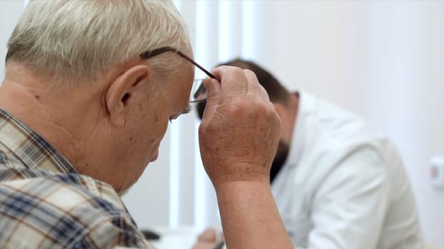 Male doctor working at the table, writing prescription. Clip. Old male patient at the hospital