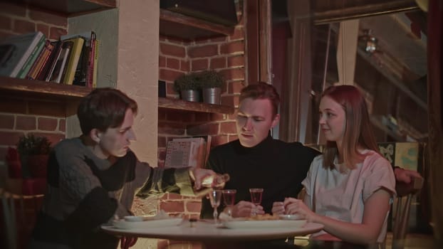 Friends spend time together at dinner at a restaurant. Media. Couple of man and woman with their male frand communicating and drinking alcohol