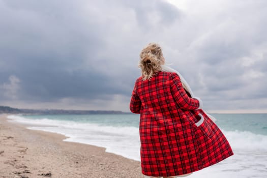 Blond woman holding Christmas tree by the sea. Christmas portrait of a happy woman walking along the beach and holding a Christmas tree in her hands. Dressed in a red coat, white dress