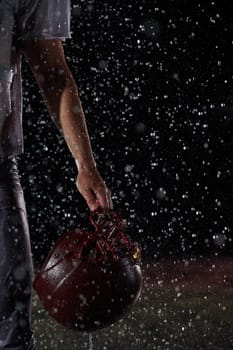 Close up of American Football Athlete Warrior Standing on a Field focus on his Helmet and Ready to Play. Player Preparing to Run, Attack and Score Touchdown. Rainy Night with Dramatic lens flare.