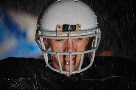 American Football Field: Lonely Athlete Warrior Standing on a Field Holds his Helmet and Ready to Play. Player Preparing to Run, Attack and Score Touchdown. Rainy Night with Dramatic Fog, Blue Light.