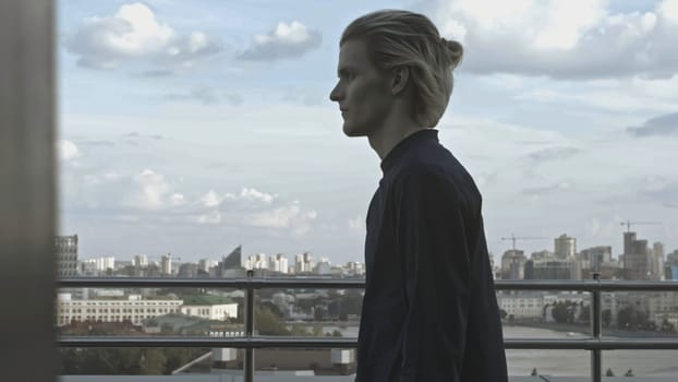 Young man on roof of building. Stock. Young man behaves strangely while on roof of building. Man on terrace of high-rise building on summer day.