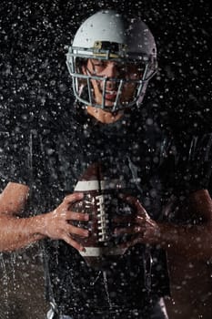 American Football Field: Lonely Athlete Warrior Standing on a Field Holds his Helmet and Ready to Play. Player Preparing to Run, Attack and Score Touchdown. Rainy Night with Dramatic Fog, Blue Light.