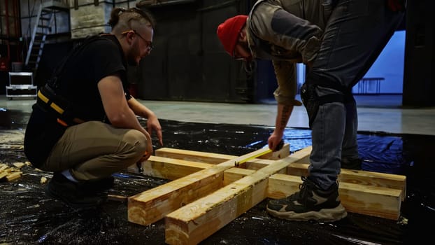 Assembly of wooden stage construction by young builders. Media. Men workers using logs for the decorations of the concert