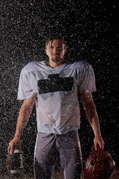 American Football Field: Lonely Athlete Warrior Standing on a Field Holds his Helmet and Ready to Play. Player Preparing to Run, Attack and Score Touchdown. Rainy Night with Dramatic Fog, Blue Light.