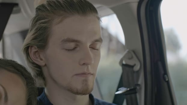 Young couple sleeps during car trip. Stock. Woman sleeps on shoulder of young man in car. Young attractive couple falls asleep during car ride.