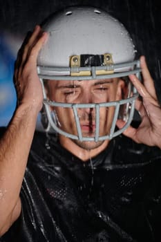 American Football Field: Lonely Athlete Warrior Standing on a Field Holds his Helmet and Ready to Play. Player Preparing to Run, Attack and Score Touchdown. Rainy Night with Dramatic Fog, Blue Light.