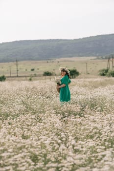 Happy woman in a field of daisies with a wreath of wildflowers on her head. woman in a green dress in a field of white flowers. Charming woman with a bouquet of daisies, tender summer photo.