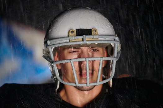 American Football Field: Lonely Athlete Warrior Standing on a Field Holds his Helmet and Ready to Play. Player Preparing to Run, Attack and Score Touchdown. Rainy Night with Dramatic Fog, Blue Light.