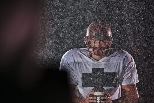 American Football Field: Lonely Athlete Warrior Standing on a Field Holds his Helmet and Ready to Play. Player Preparing to Run, Attack and Score Touchdown. Rainy Night with Dramatic Fog, Blue Light.