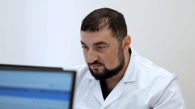 Middle aged doctor with in clinic. Clip. Bearded man in white coat looking at computer monitor