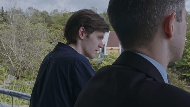 Two young men standing on balcony and communicating. Stock clip. Business partners discussion and green spring vegetating on the background