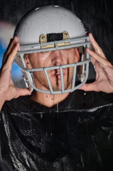 American Football Field: Lonely Athlete Warrior Standing on a Field Holds his Helmet and Ready to Play. Player Preparing to Run, Attack and Score Touchdown. Rainy Night with Dramatic Fog, Blue Light.