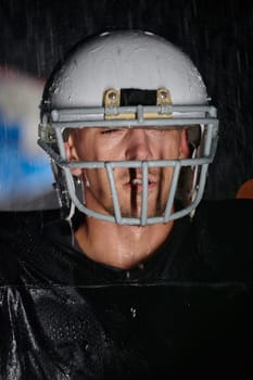 American Football Field: Lonely Athlete Warrior Standing on a Field Holds his Helmet and Ready to Play. Player Preparing to Run, Attack and Score Touchdown. Rainy Night with Dramatic Fog, Blue Light.