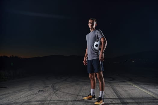 Portrait of a young handsome soccer player man on a street playing with a football ball