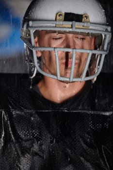 American Football Field: Lonely Athlete Warrior Standing on a Field Holds his Helmet and Ready to Play. Player Preparing to Run, Attack and Score Touchdown. Rainy Night with Dramatic Fog, Blue Light.