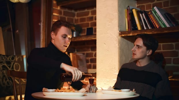 Two friends are sitting in restaurant, chatting and drinking alcoholic drink. Media. Two young men are drinking alcoholic tincture in restaurant. Cozy meeting of two friends in restaurant with alcoholic drink.