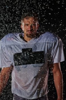 American Football Field: Lonely Athlete Warrior Standing on a Field Holds his Helmet and Ready to Play. Player Preparing to Run, Attack and Score Touchdown. Rainy Night with Dramatic Fog, Blue Light.