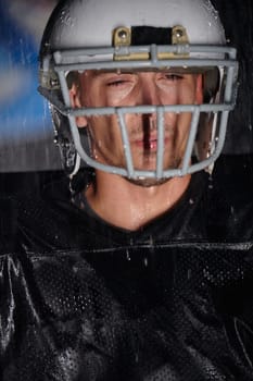 American Football Field: Lonely Athlete Warrior Standing on a Field Holds his Helmet and Ready to Play. Player Preparing to Run, Attack and Score Touchdown. Rainy Night with Dramatic Fog, Blue Light.