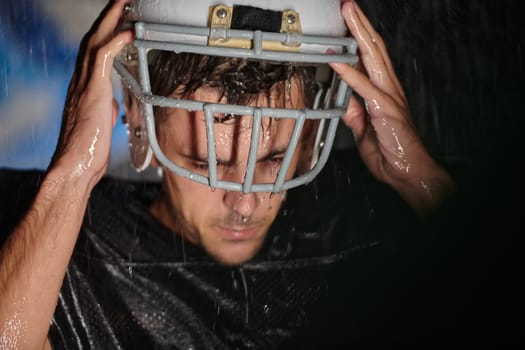 American Football Field: Lonely Athlete Warrior Standing on a Field Holds his Helmet and Ready to Play. Player Preparing to Run, Attack and Score Touchdown. Rainy Night with Dramatic Fog, Blue Light.