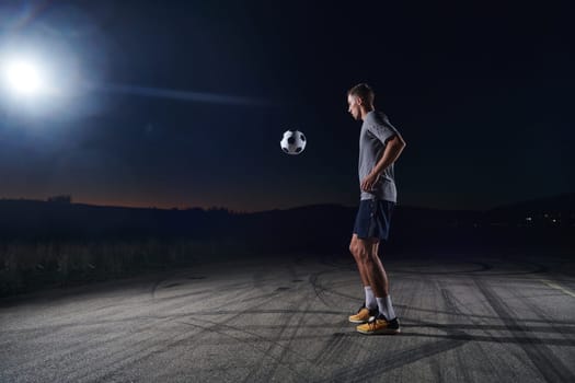 Portrait of a young handsome soccer player man on a street playing with a football ball.