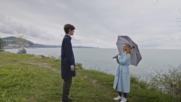 Young couple dating by the ocean shore and communicating. Stock clip. Man and woman spend time outdoors on a cold windy day