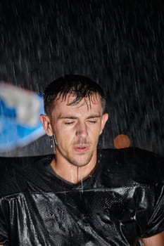 American Football Field: Lonely Athlete Warrior Standing on a Field Holds his Helmet and Ready to Play. Player Preparing to Run, Attack and Score Touchdown. Rainy Night with Dramatic Fog, Blue Light.