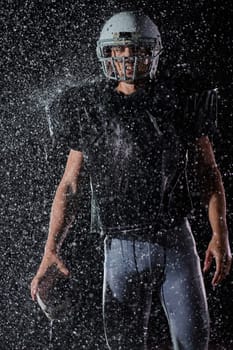 American Football Field: Lonely Athlete Warrior Standing on a Field Holds his Helmet and Ready to Play. Player Preparing to Run, Attack and Score Touchdown. Rainy Night with Dramatic Fog, Blue Light.