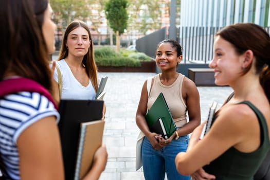African American female university student talking to friends in a circle standing outside in college campus. Friendship and education concepts.