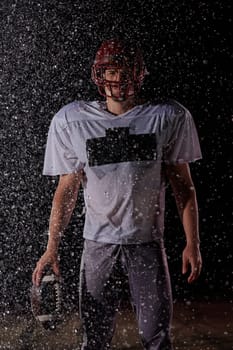 American Football Field: Lonely Athlete Warrior Standing on a Field Holds his Helmet and Ready to Play. Player Preparing to Run, Attack and Score Touchdown. Rainy Night with Dramatic Fog, Blue Light.