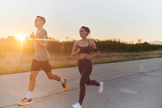 A handsome young couple running together during the early morning hours, with the mesmerizing sunrise casting a warm glow, symbolizing their shared love and vitality.