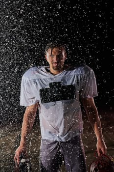 American Football Field: Lonely Athlete Warrior Standing on a Field Holds his Helmet and Ready to Play. Player Preparing to Run, Attack and Score Touchdown. Rainy Night with Dramatic Fog, Blue Light.