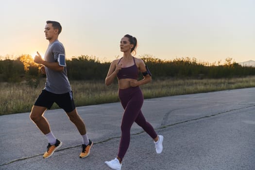 A handsome young couple running together during the early morning hours, with the mesmerizing sunrise casting a warm glow, symbolizing their shared love and vitality.