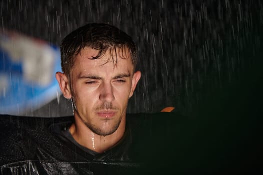 American Football Field: Lonely Athlete Warrior Standing on a Field Holds his Helmet and Ready to Play. Player Preparing to Run, Attack and Score Touchdown. Rainy Night with Dramatic Fog, Blue Light.