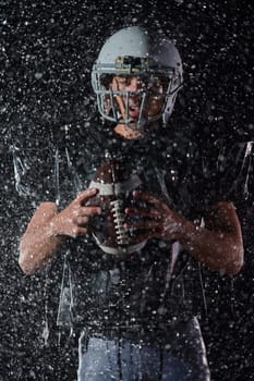 American Football Field: Lonely Athlete Warrior Standing on a Field Holds his Helmet and Ready to Play. Player Preparing to Run, Attack and Score Touchdown. Rainy Night with Dramatic Fog, Blue Light.